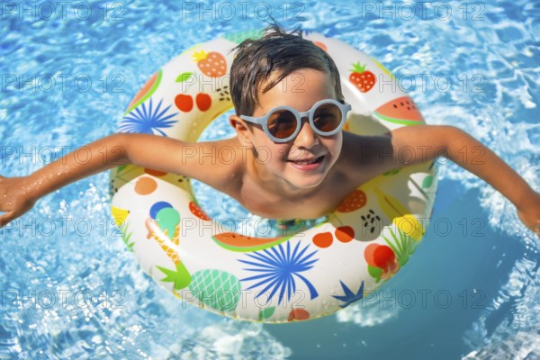 Top view of a happy young boy inside a blue swimming pool with swim goggles and a float
