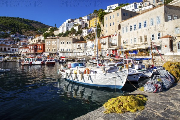 Fishing and recreational boats in harbor of Hydra island. Houses of Hydra town with tiled roofs on steep hill in fantastic summer morning on the Greek islands. a fish net lies on the pier