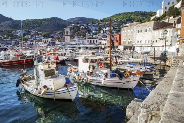 Amazing Hydra town and harbor with white fish boats and pleasure boats on island Hydra with steep slope and street on it with cargo donkeys. Unrecognizable person in distance