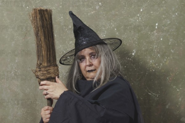 Old witch with white hair and a black hat with an ancient broom in her hands