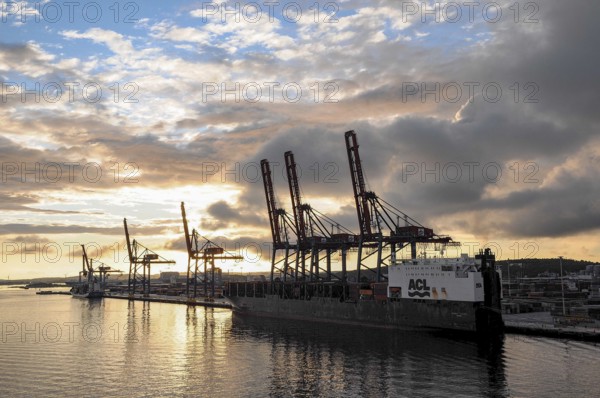 Harbour at sunset with cranes and a large ship, clouds in the sky are reflected in the water, Gothenburg, Baltic Sea, Sweden, Europe