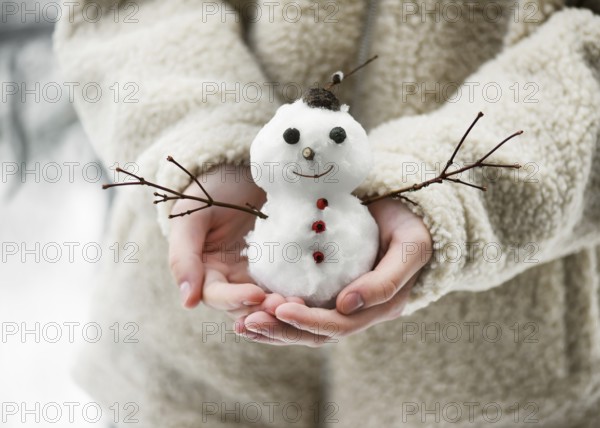 Little snowman, decorated with twigs and berries, held in children's hands in a winter garden with lots of snow. Winter atmosphere