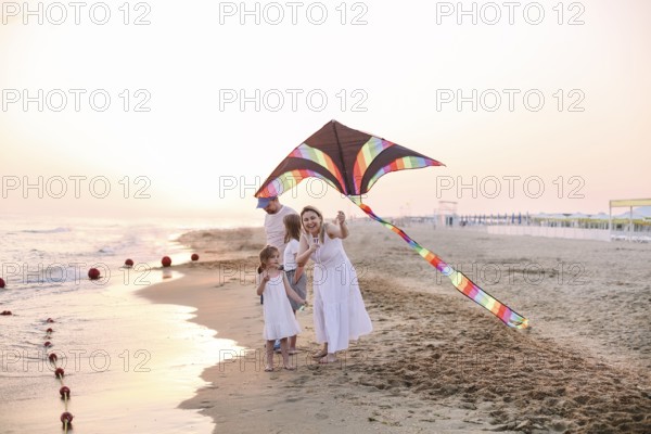 Happy family with parents and kids playing together with snakes on a beach vacation. Summer happiness concept with Mixed-race people having fun by the sea