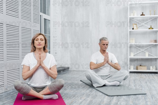 Senior couple meditating with praying hands yoga mat home