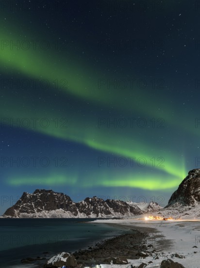 Spectacular dancing green strong northern lights over the famous round boulder beach near Uttakleiv on the Lofoten islands in Norway on clear winter night with snow-clad mountains