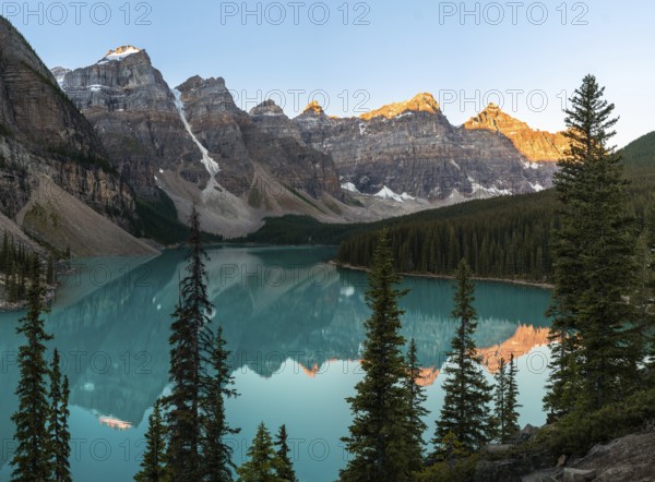 Sunset over a serene lake surrounded by rocky mountains and pine trees, with reflections in the clear water, Moraine Lake, Banff National Park, Canadian Rockies