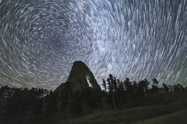 Star Trails over Devils Tower Butte at Night. Light Flare of Climbers on a Wall. Wyoming, USA, North America