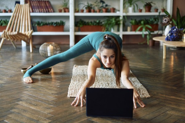 Young sporty woman practicing yoga at home watching online exercises on her laptop. Healthy lifestyle concept