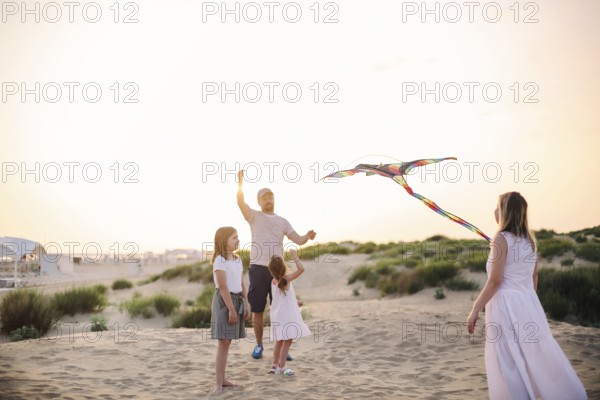 Happy family with parents and kids playing together with snakes on a beach vacation. Summer happiness concept with Mixed-race people having fun by the sea