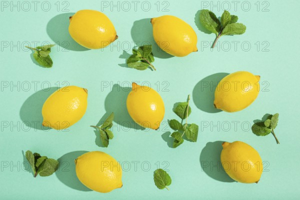 Fresh yellow lemons with mint on minimal blue background on bright sun light with hard shadows pattern summer background flat lay from above, citrus food composition, space for text
