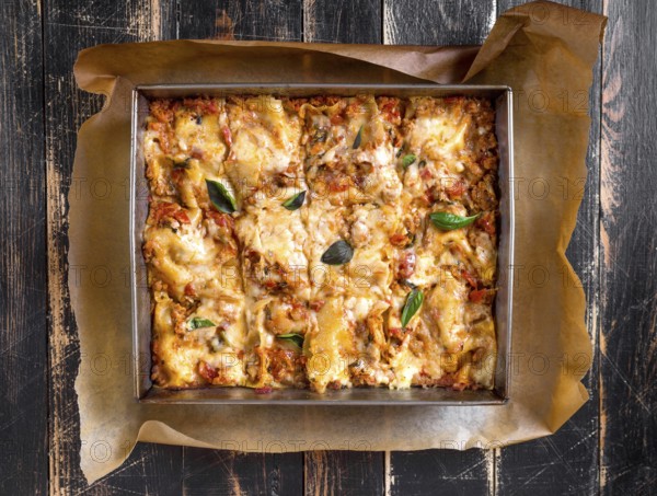Top view of a delicious traditional italian lasagna made with minced beef bolognese sauce topped with basil leafs served on a rustic dark wooden table