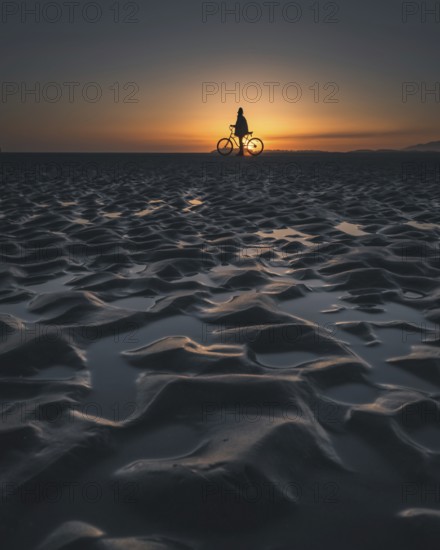 Silhouette of a person with a bicycle on a beach during a picturesque sunset, Tofino, BC, Canada, North America