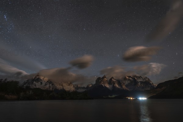 Night sky filled with stars over snow-capped mountains and a calm lake, with clouds and reflections creating a serene atmosphere, Torres Del Paine, Patagonia