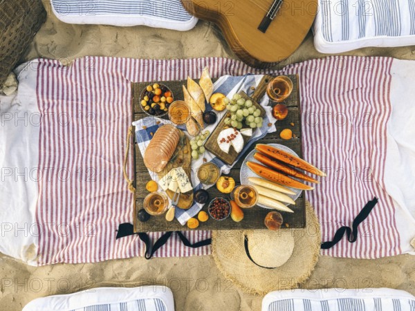 Various tasty food and drinks placed on wooden table during summer picnic on sandy beach at sunset