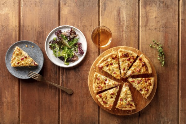 An overhead photo of a quiche with wine and mesclun salad leaves on a dark rustic wooden background with copy space