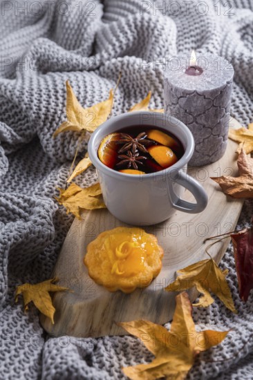 Cosy and soft winter background, with mulled wine, knitted blanket and candle with lemon cake on vintage wooden board. Christmas holidays at home
