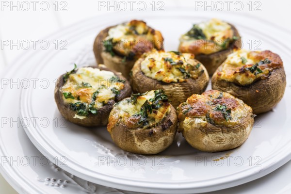 Baked champignons mushrooms, filled with cheese, parsley and roasted garlic on white plate. Selective focus. Healthy food concept