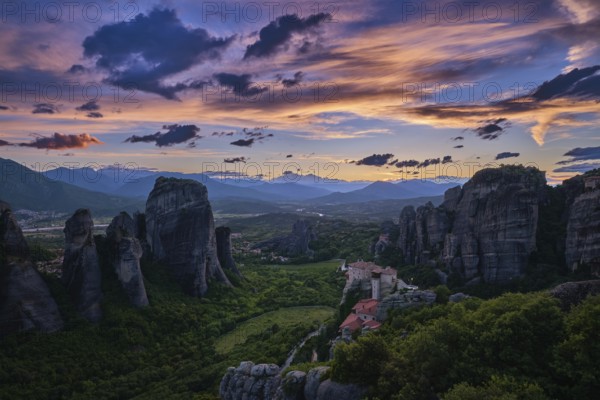 Twilight view of Meteora valley. Valley in last moments of sunlight, hazy distant mountains, clifftop Moni Agias Varvaras Roussanou nunnery and rocks and cliffs. Beautiful sky in sunset colors, colorful clouds. Greece, UNESCO World Heritage