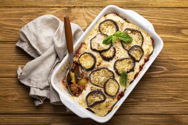 Greek mediterranean dish Moussaka with baked eggplants, ground beef in white ceramic casserole with napkin on wooden rustic background from above, traditional dish of Greece