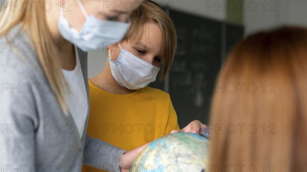 Female teacher with medical mask teaching geography with globe classroom