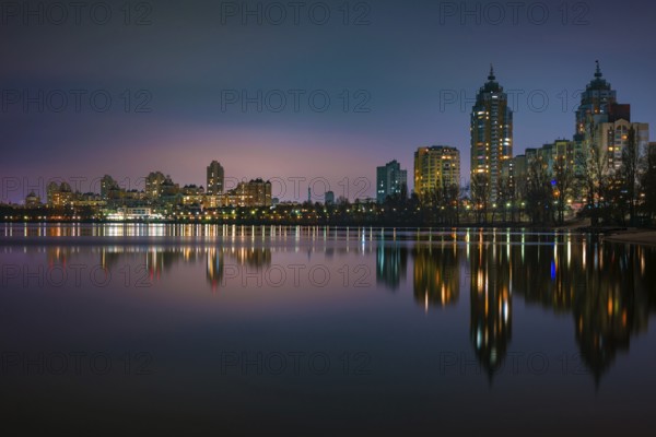 Night view of modern buildings in the Obolon district of Kiev, Ukraine, close to the Dnieper River, The lights reflect on the calm water, Europe
