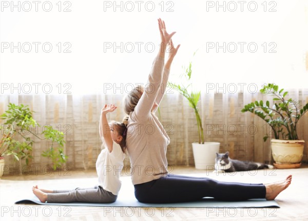 Mature woman and little girl sitting on mat in lotus pose and meditating while doing yoga in spacious room at home together