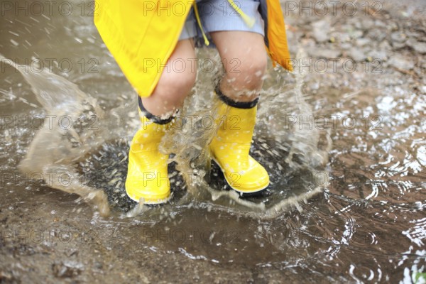 Little girl wearing yellow boots and coat jumping in rainy day