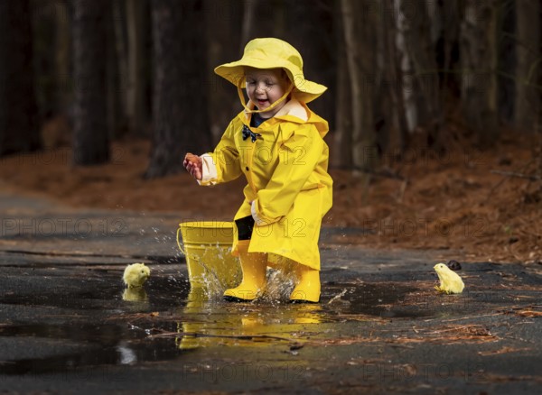 A small child plays in the rain while little chicks try to get a drink of water