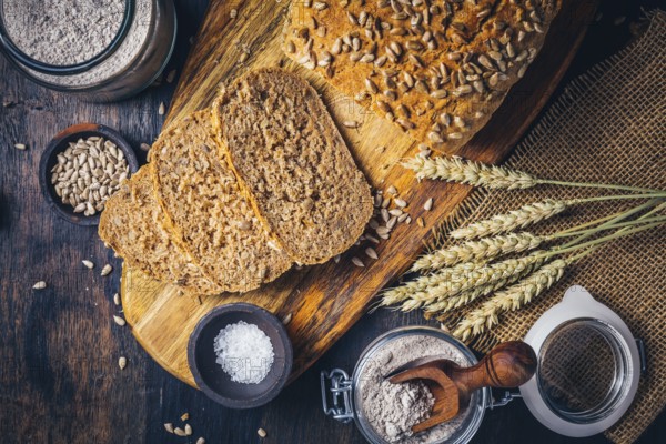 Homemade wholemeal spelt bread with sunflower seeds and baking ingredients on wooden background