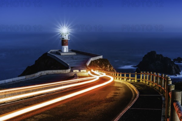 Bright trailing car lights lead to Cabo Ortegal lighthouse at night