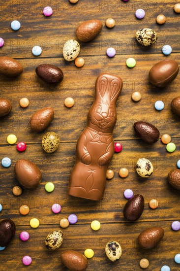 Chocolate Easter bunny with sweet chocolate eggs and colorful sweets on wooden background