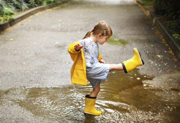Little girl wearing yellow boots and coat jumping in rainy day