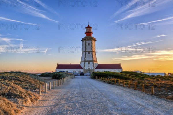 Beautiful of coastal lighthouse in warm colors of sunset, a clear path leading to it. Clear blue sky and some clouds, sun down over horizon, tranquil scene. Navigation beacon, safety for ships and small vessels, Atlantic ocean coast landscape