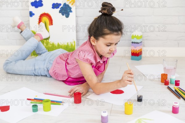 Little girl lying floor painting with water color with paint brush paper