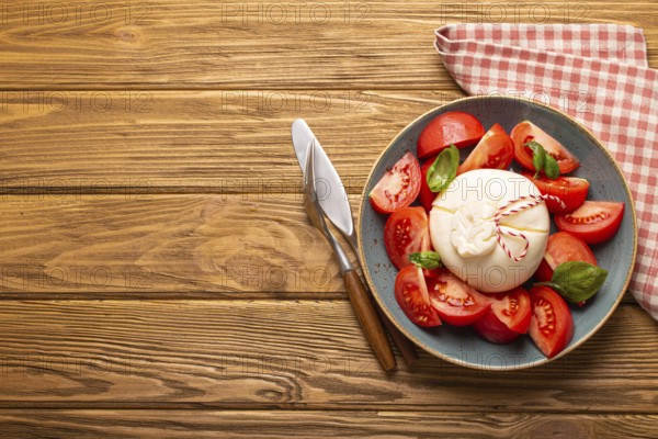 Italian salad with fresh tomatoes, burrata cheese, basil and olive oil served on ceramic plate on rustic wooden background from above, healthy snack or lunch with space for text