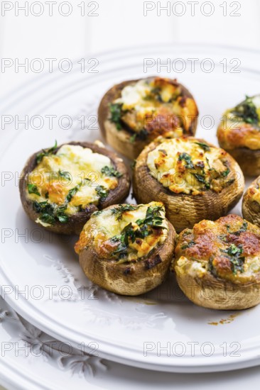Baked champignons mushrooms, filled with cheese, parsley and roasted garlic on white plate. Selective focus. Healthy food concept