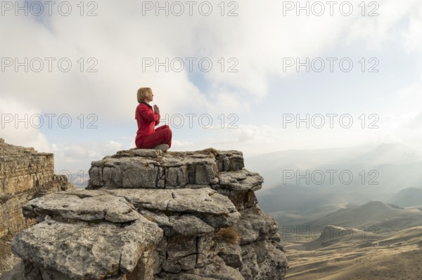 A beautiful girl meditates in a lotus pose sitting on a rock above the clouds against the backdrop of the setting sun and sunset