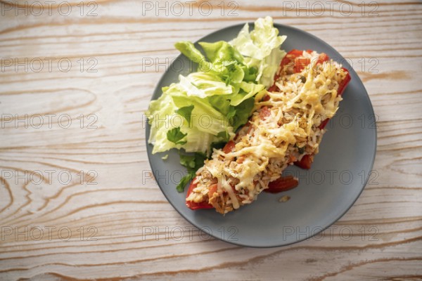 Pointed red bell pepper baked with rice, tuna and cheese, lettuce salad with parsley garnish on a gray blue plate, rustic wooden table, copy space, high angle view from above, selected focus