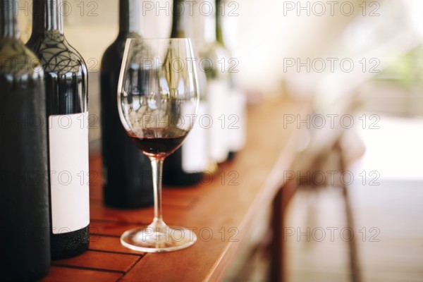 Wine bottles and glass with red wine on wooden table on the garden background in sunny day party