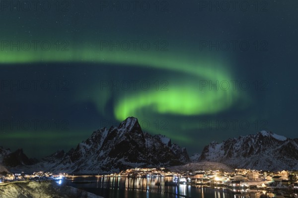 Dancing green polar lights over the village Reine on the Lofoten islands in Norway at night in winter with snow capped mountains