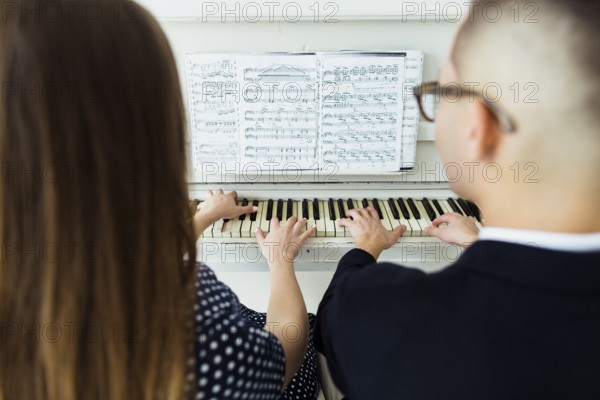 Close up couple playing piano with musical sheet