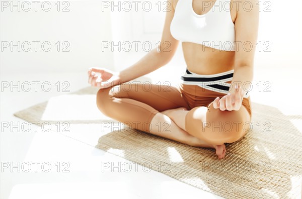 Back view of unrecognizable female in sportswear sitting with crossed legs and mudra hands on mat and doing yoga while practicing mindfulness
