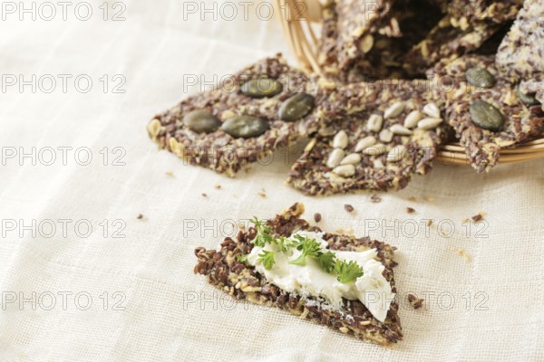 Healthy snacks from linseed, oat, herbs and various seeds, one with cream cheese and parsley garnish on a light beige napkin, copy space, selected focus, narrow depth of field
