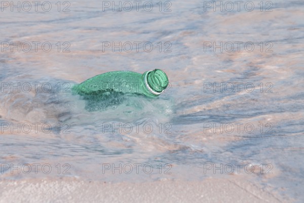 A green plastic bottle floating in the clear ocean water, indicating pollution