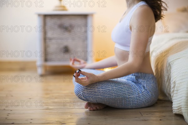 Smiling young brown haired woman in pajamas practicing yoga in bright bedroom in the morning