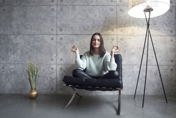 Portrait of attractive brunette woman in green sweater sitting on armchair trying to relax
