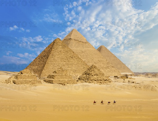 All Egyptian Pyramids from distance with row of camels walking in foreground in Giza, Cairo, Egypt. Wide telephoto shot plenty of copy space