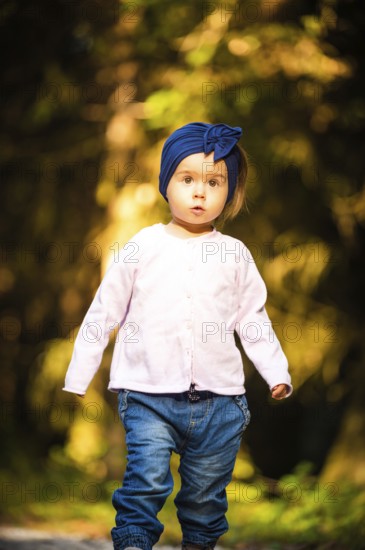 Portrait of 2 years old baby girl in forest walking by herself. Not wanting to follow parents. Concept of child independence