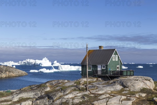 Qeqertarsuaq, Greenland, July 05, 2018: A green wooden house with icebergs in the background, North America