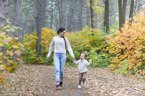 Mother and daughter play in autumn park. Parent and child walk in the forest on a fall day. Mom hugging kid
